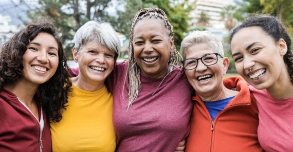 Five people of different ages and backgrounds smiling together outdoors.