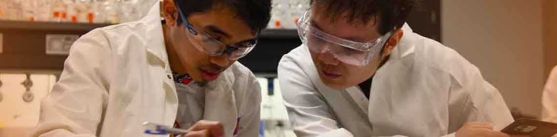 Two people in lab coats at a table working together